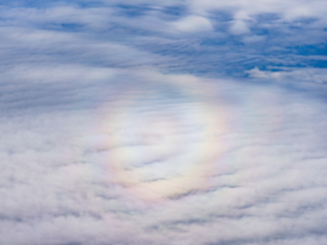 飛行機の窓から見える円形の虹(全円虹)と雲の風景